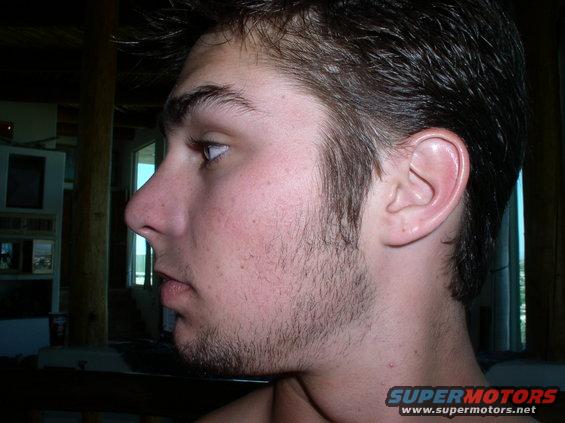 Profile of a young man with short dark hair and stubble, wearing a Supermotors.net t-shirt