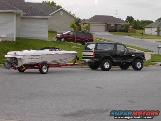 White Four Winns 191 Unlimited boat on trailer towed by black SUV. Side view