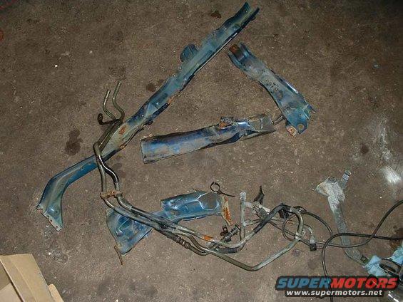 Several blue metal car frame pieces and fuel lines scattered on a concrete floor