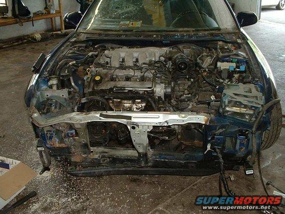 Car's engine bay, front bumper and grille are missing, showing the engine and internal components