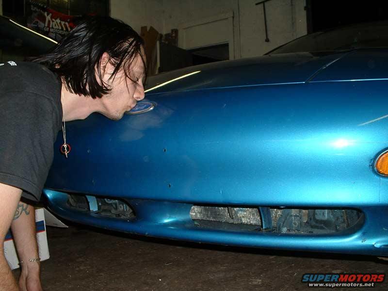 Man kissing the Ford emblem on the front of a blue car