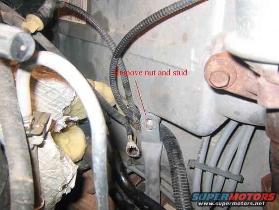 Close-up of engine bay with wires, hoses, and a bracket labeled 'Remove nut and stud'