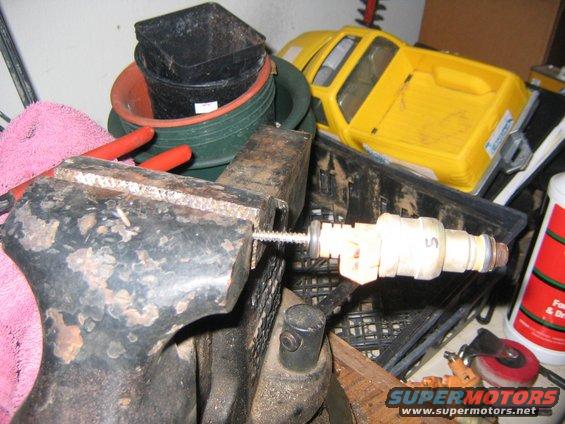 Fuel injector clamped in a vise with a screw going through it. A yellow toy truck is in the background