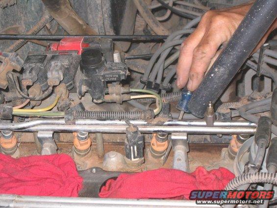 Engine fuel injectors with red rags underneath. A hand is working on the engine