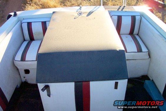 Interior of a boat with white seats with red and black stripes. There's a dark table in the middle