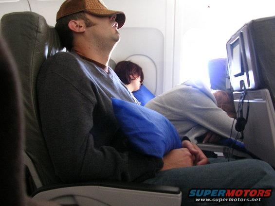 People sleeping in airplane seats with pillows and overhead lights on