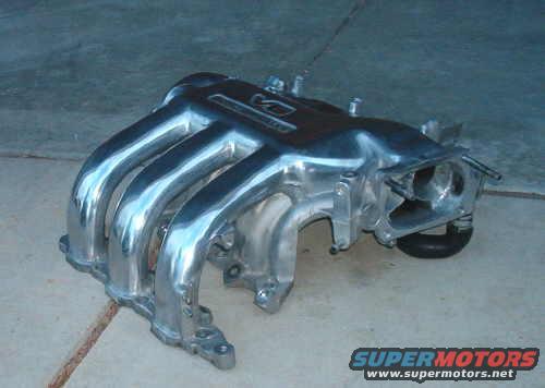 Polished aluminum intake manifold with four runners, resting on a concrete floor