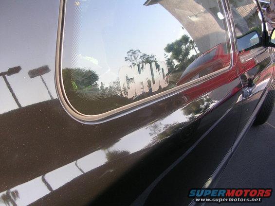 Close-up of a dark car's side door and rear window with a white "CHUD" sticker