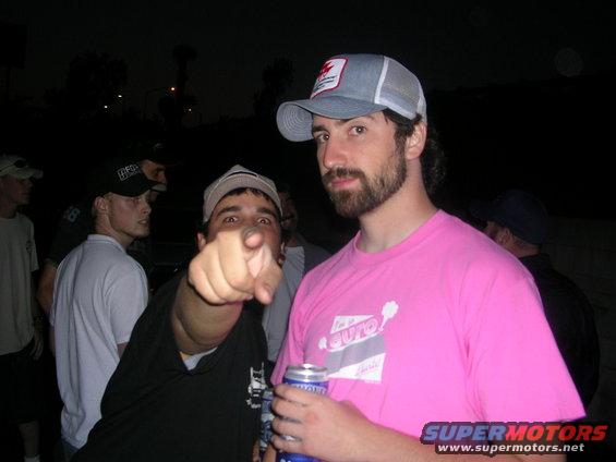 Guy in pink shirt with beard and cap, another guy pointing at camera, others in background at night