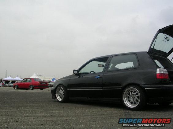 Black hatchback car with open trunk, aftermarket wheels, parked on asphalt