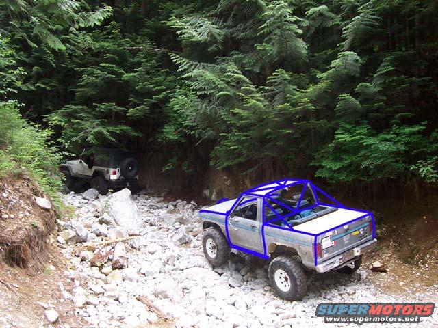 pickup truck with blue roll cage on rocky trail, another jeep in background