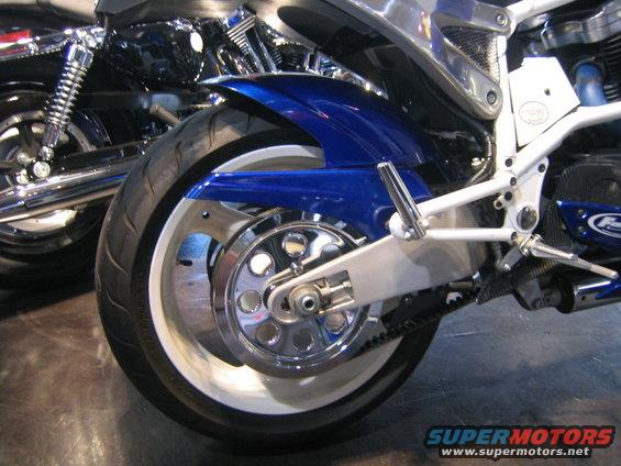 Motorcycle rear wheel with chrome accents and blue fender. Another motorcycle is visible behind it