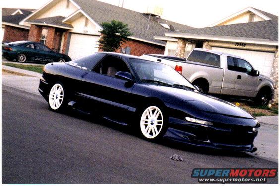 dark blue sports coupe with white rims parked on street, silver pickup truck and green Acura in background