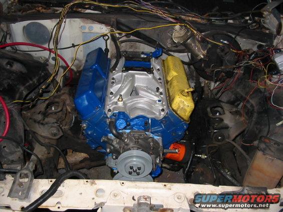 Engine bay with a blue and yellow V8 engine, lots of wires, and an orange oil filter