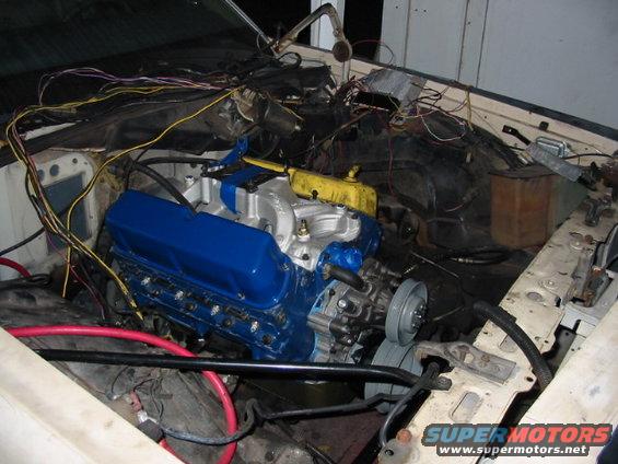 Engine bay with a blue engine, red cables, and complex wiring. The vehicle appears to be under repair