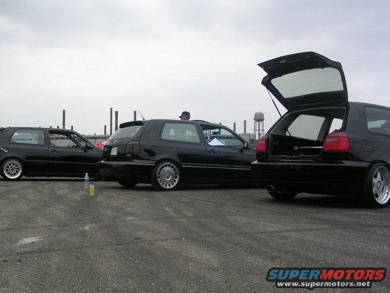 Three black hatchbacks parked outside, one with its trunk open