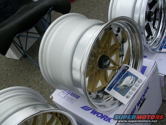 Three polished car wheels with gold spokes and chrome lips, one with a product brochure