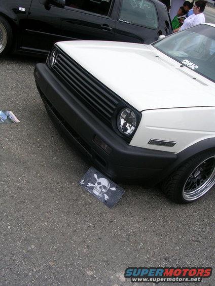 White VW Golf GTI parked next to a black car. Skull and crossbones sticker on the ground