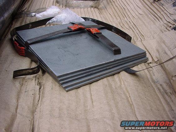 Stack of flat metal plates secured with straps and orange clamps