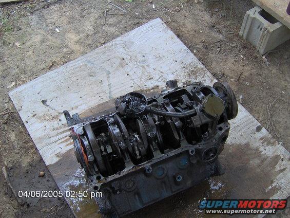 engine block with crankshaft and pistons visible, sitting on a wooden board outdoors