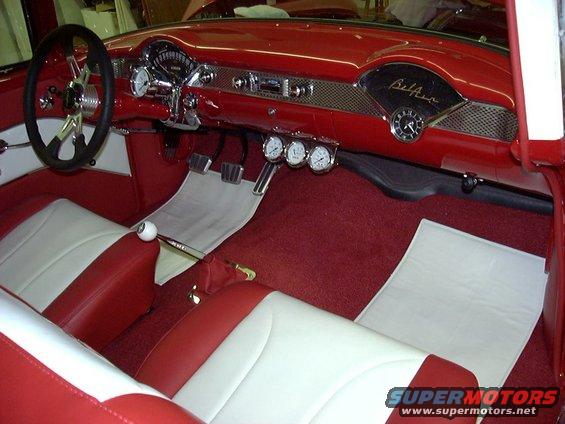 Interior view of a red and white 1955 Chevrolet with custom gauges and a floor shifter