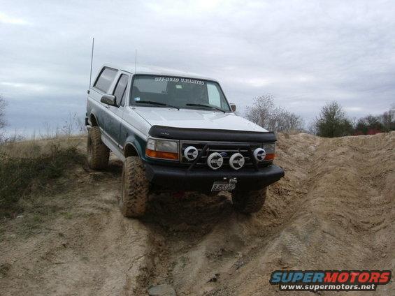 1996 Ford Bronco climbing a dirt hill with off-road lights