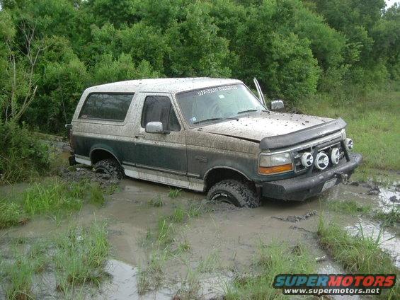 Muddy 1996 Ford Bronco stuck in a muddy ditch with trees in the background