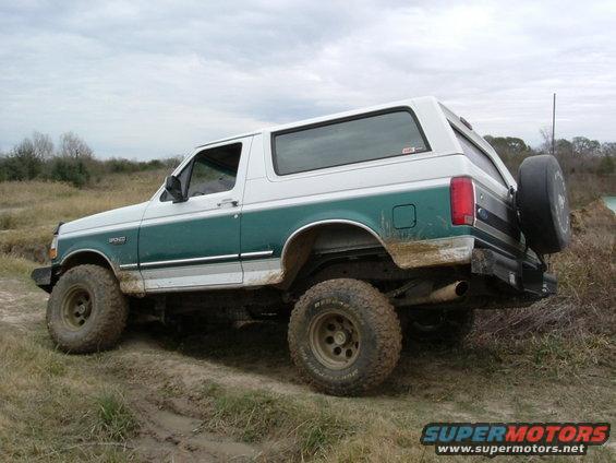 White and green Ford Bronco with off-road tires on a muddy trail