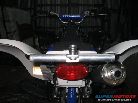 Rear view of a quad bike with a red taillight, silver exhaust, and white fenders. Handlebars with 'RENTHAL' visible