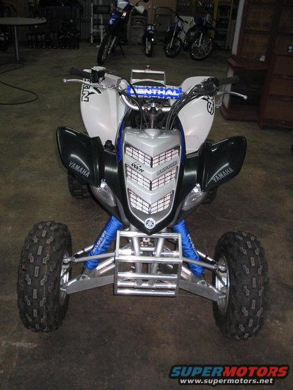 Front view of a white and black Yamaha Raptor ATV with blue suspension components