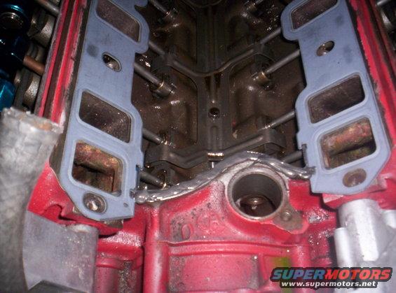 Engine block with intake manifold gaskets installed. The red block has two grey gaskets with multiple openings