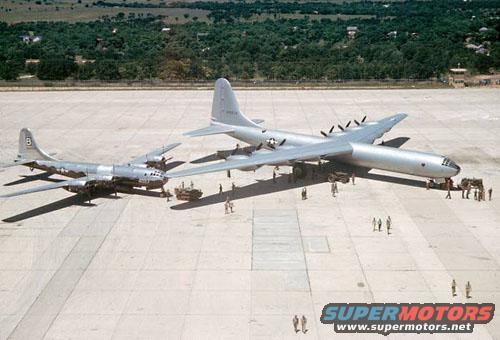 Two large military airplanes parked on an airfield with people and vehicles nearby