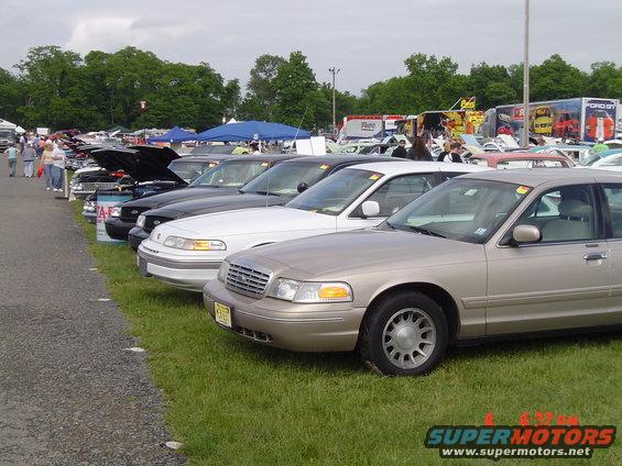 Tan 1998 Ford Crown Victoria, 3/4 front view, parked in a row at an outdoor event