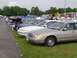 1999 Ford Crown Victoria - A row of sedans, including a tan 1998 Ford Crown Victoria, are parked on a grassy field under a cloudy sky.