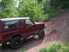 1994 Ford Bronco - A maroon Ford Bronco navigates a steep, rocky dirt path surrounded by trees.