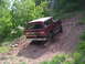1994 Ford Bronco - A red 1994 Ford Bronco navigates a steep, dusty off-road trail surrounded by trees.