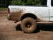 1994 Ford Bronco - White pickup truck covered in mud after driving off-road. The rear wheel and fender are heavily soiled.