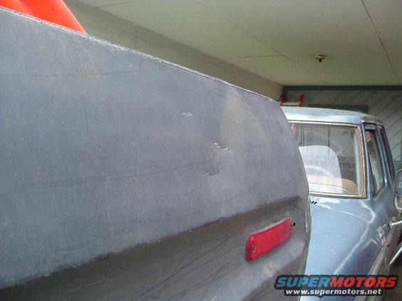 Gray rear quarter panel with red reflector, next to a blue truck cab