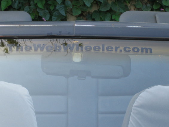 Car interior with "TheWebWheeler.com" text on windshield and grey seat covers
