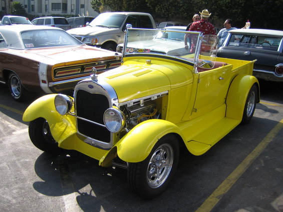 Yellow 1928 Ford Model A roadster pickup truck with chrome grille and exposed engine, parked in a lot