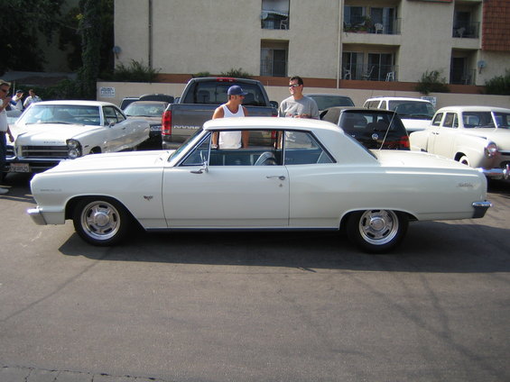 White 1964 Chevelle Malibu coupe parked, two guys standing by it