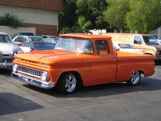 Orange pickup truck parked in a lot with other cars and a van behind it