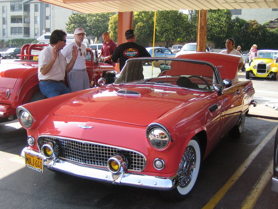 Red 1955 Ford Thunderbird convertible with wire wheels and yellow fog lights. License plate MAJ 640. Two men talking next to it