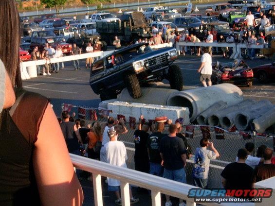 Modified Ford Bronco attempting an obstacle course over concrete pipes, with spectators watching