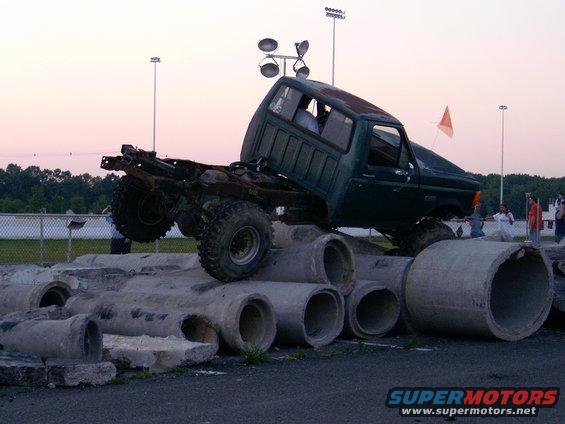 Green pickup truck with lifted suspension and large tires is on top of concrete pipes. It looks like a 1986 Ford F-250