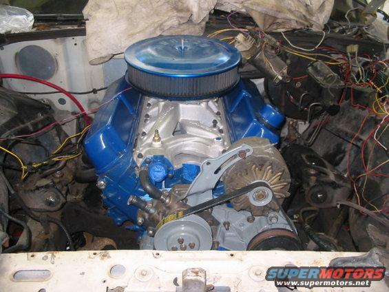 Close-up of a blue V8 engine with a chrome air cleaner in an engine bay. Wires and engine parts are visible