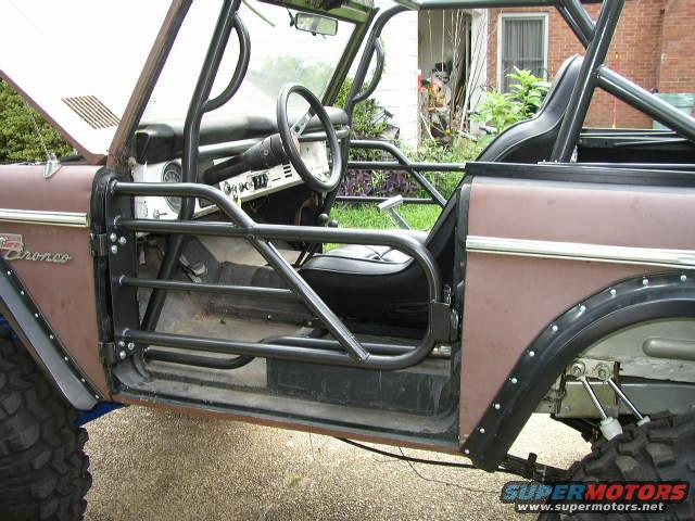 Side view of a modified Ford Bronco with a roll cage and no doors. The hood is up