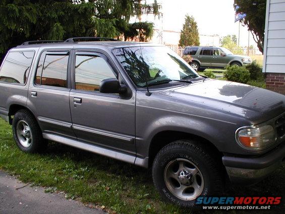 Gray Ford Explorer parked on grass, another green SUV in background