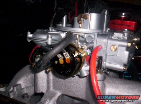 Close-up of a carburetor mounted on an intake manifold, with red fuel lines