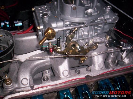 Close-up of a carburetor and intake manifold with linkage and fuel line